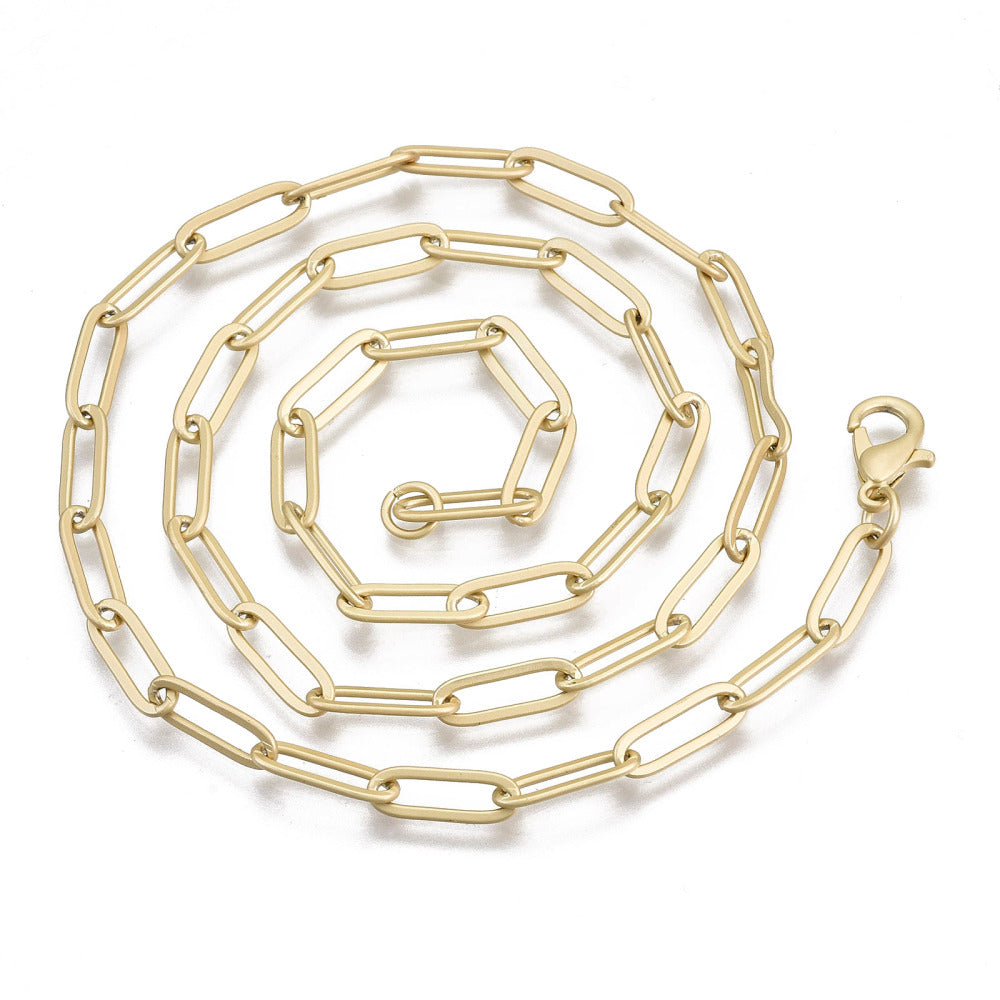 matte golden large paperclip link necklace with lobster claw clasp in swirl pattern over white background. 