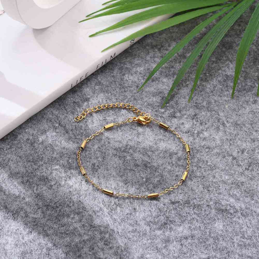 golden satellite tube chain bracelet with lobster claw clasp and extender on gray fabric background with green leaves. 