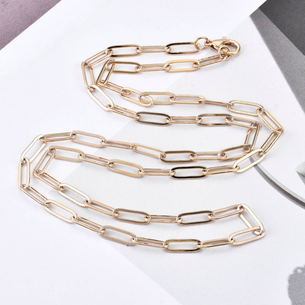 golden small paperclip link necklace with lobster claw clasp on white and gray photo background. 