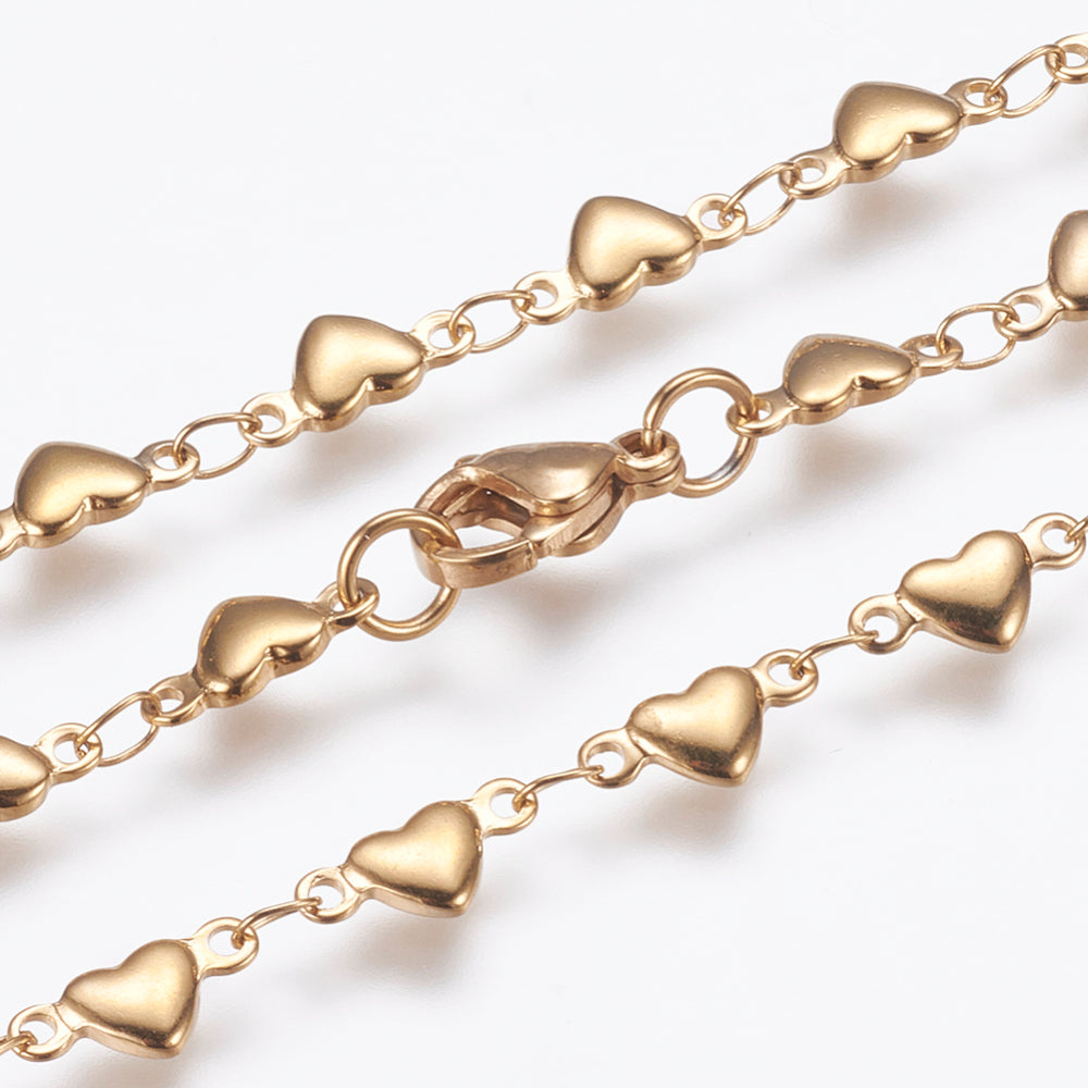 zoomed in sections of golden flat heart link necklace with lobster claw clasp on white background. 
