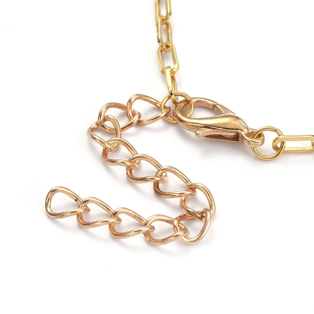 zoomed in section of golden lobster claw clasp and extender chain on golden paperclip chain with white background. 