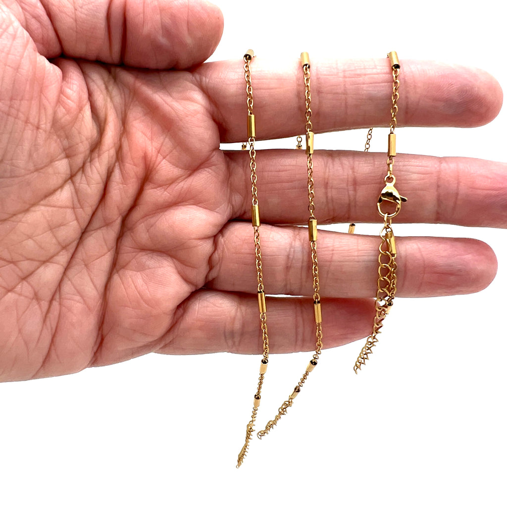 golden satellite tube chain bracelet with lobster claw clasp and extender on a hand against white background. 