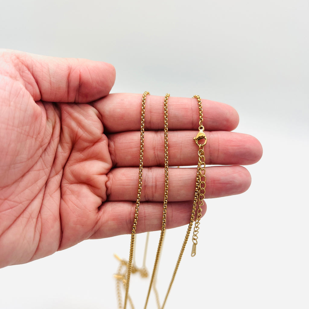 golden Rolo chain necklace with lobster claw clasp and extender chain draped a hand with white background. 