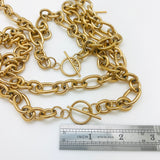 two golden Rolo chain necklaces with toggle clasp above a stainless steel imperial ruler on a white background. 