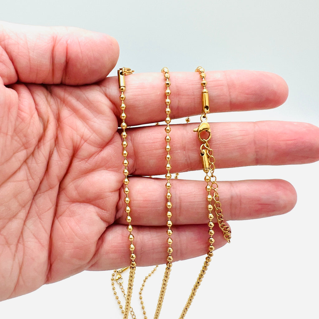 golden ball chain with lobster claw clasp and extender chain draped over hand with white background. 