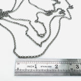 stainless steel medium Rolo chain necklace with lobster claw clasp above a stainless steel imperial ruler  on white background. 