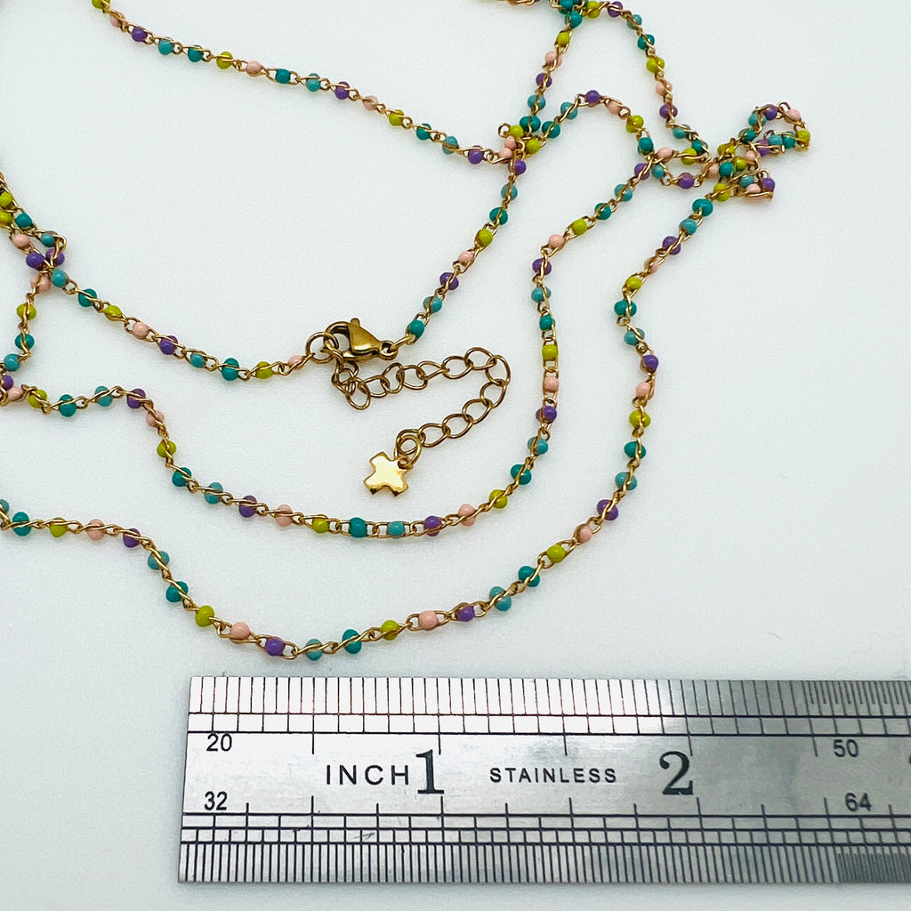 golden multi-color enamel twisted chain necklace with lobster claw clasp extender chain and cross charm displayed over a ruler with a white background. 