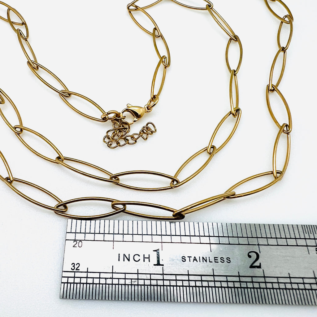 golden marquise paperclip chain necklace with lobster claw clasp and extender chain above stainless steel ruler on white background. 
