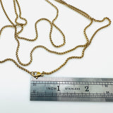 golden squared Rolo chain necklace with lobster claw clasp above stainless steel imperial ruler on white background. 