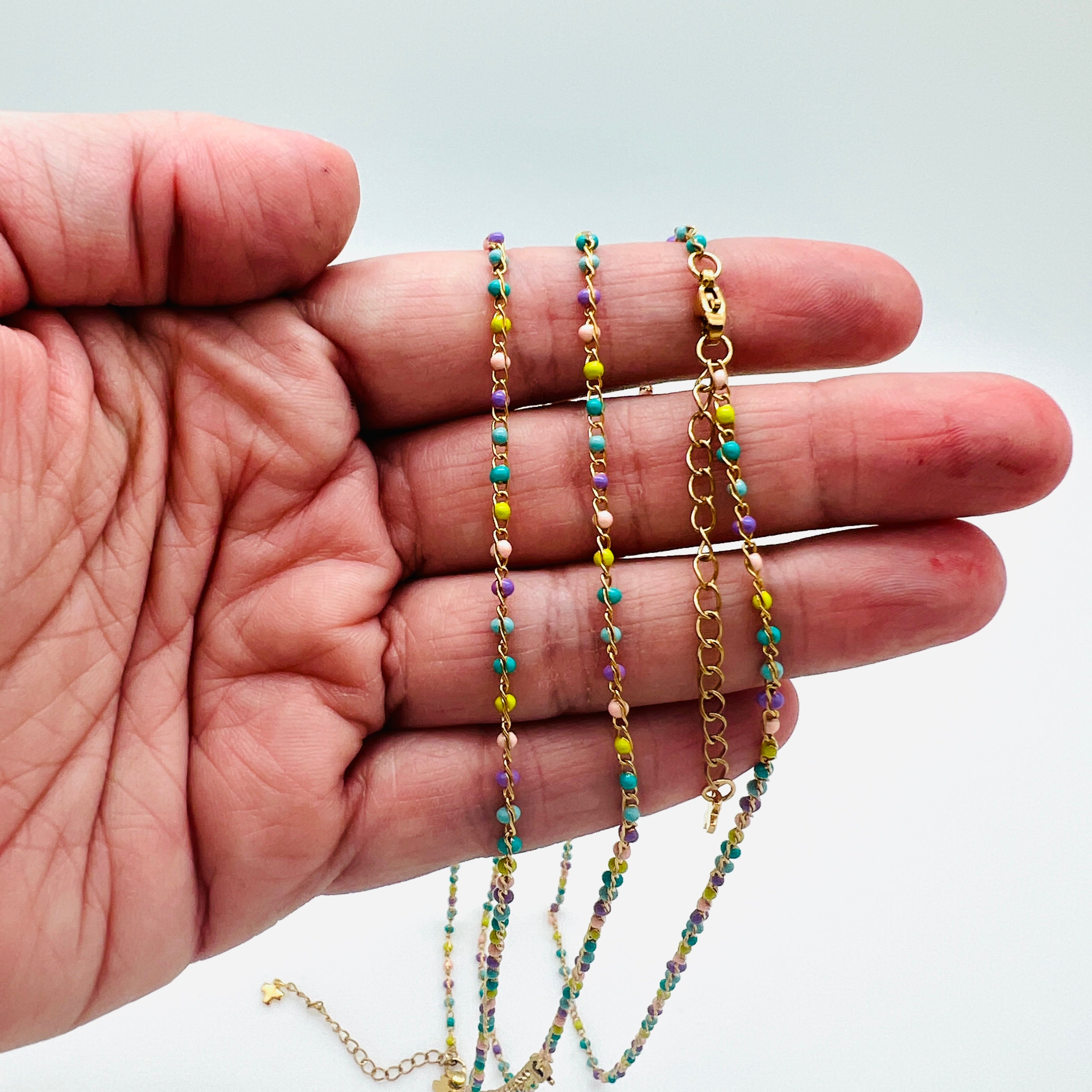 golden multi-color enamel twisted chain necklace with lobster claw clasp extender chain and cross charm draped over a hand with white background. 