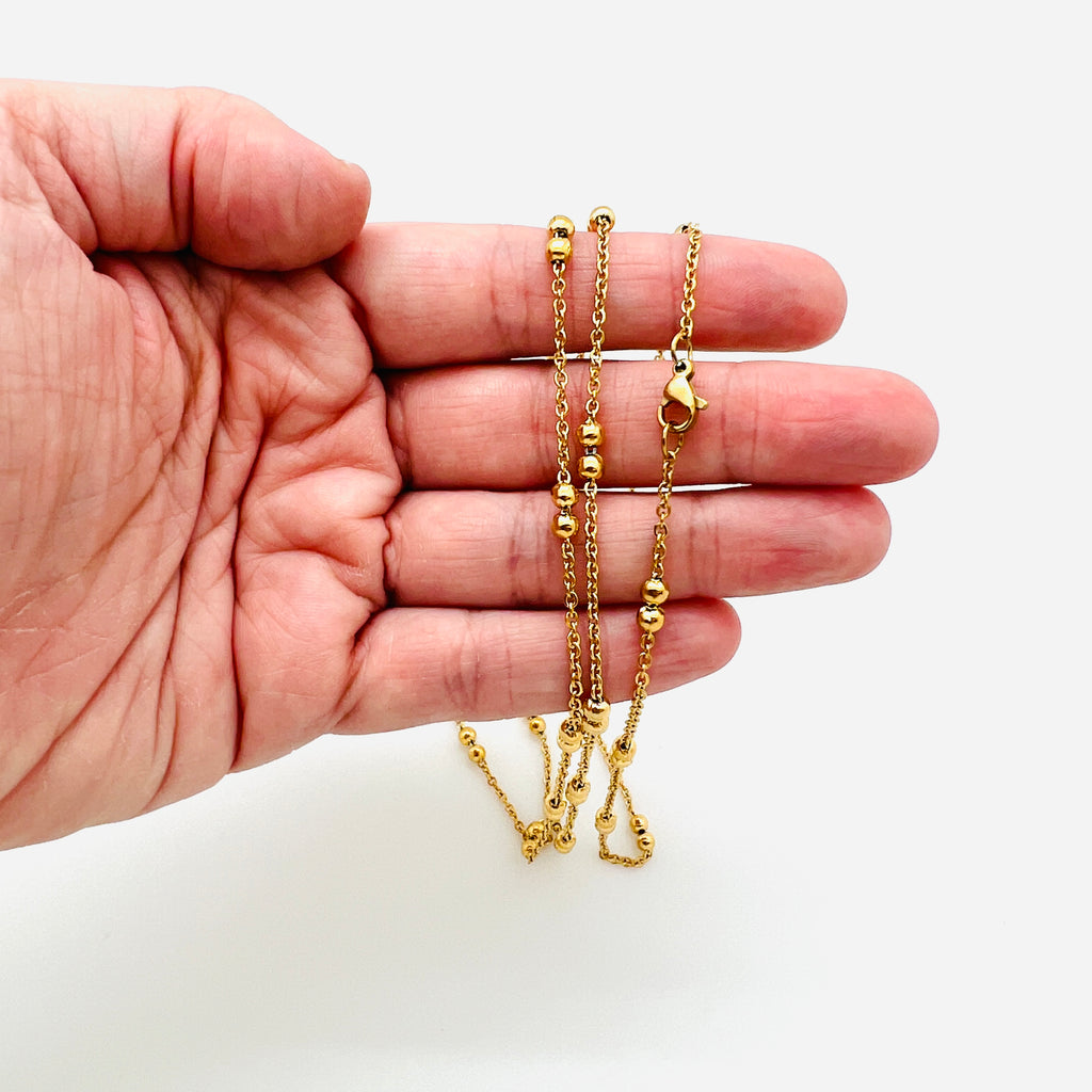 golden cable link double satellite chain necklace with lobster claw clasp draped over a hand with a white background. 
