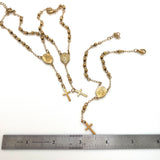 three golden rosary bracelets displaying both the back and front views of the oval medals displayed above a stainless steel imperial ruler on a white background