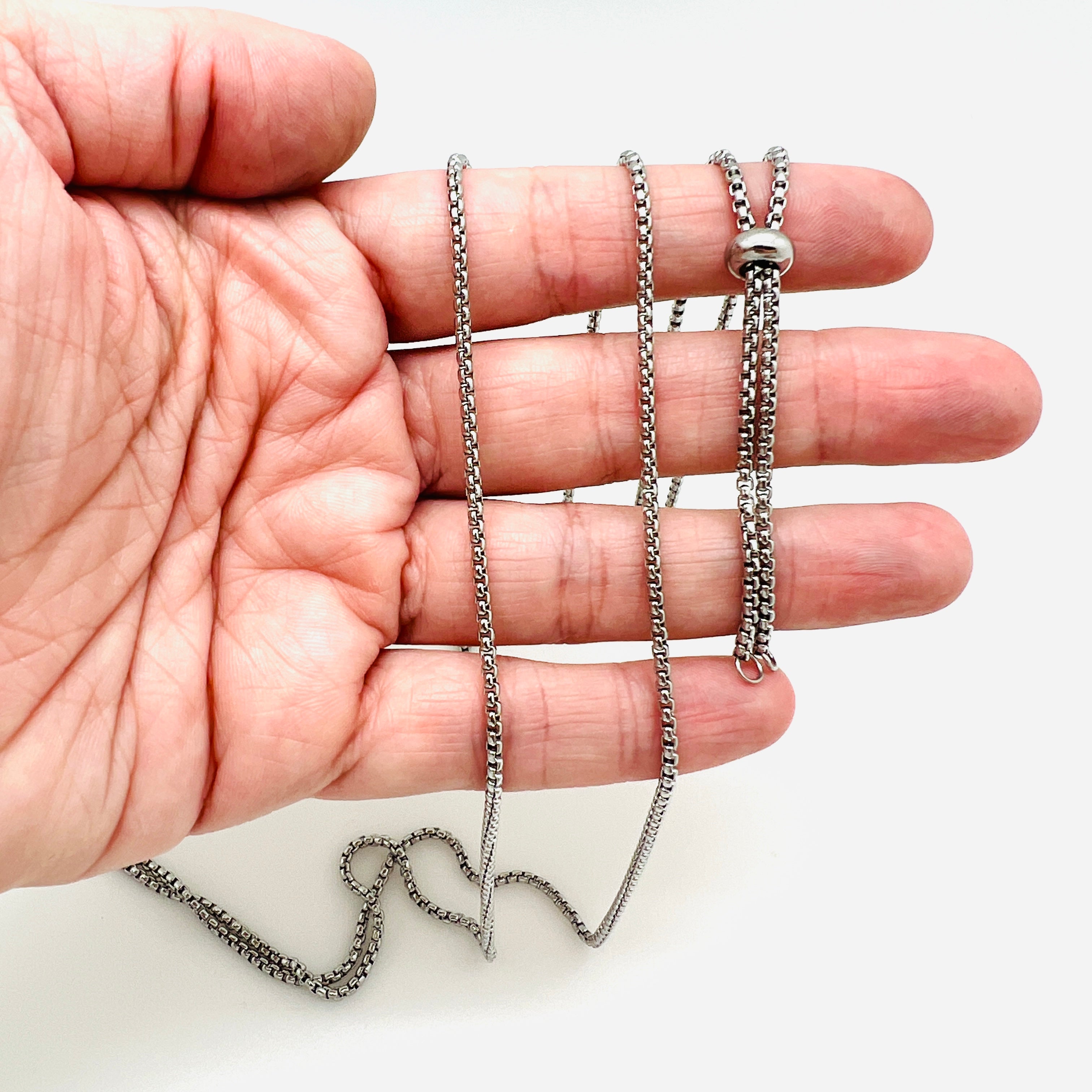 stainless steel adjustable venetian box chain Bolo necklace with slider bead displayed on a hand with white background. 