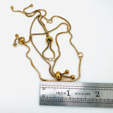 10 inch adjustable, golden plated, stainless steel slider bracelet with slider stopper beads shown above an imperial ruler. 