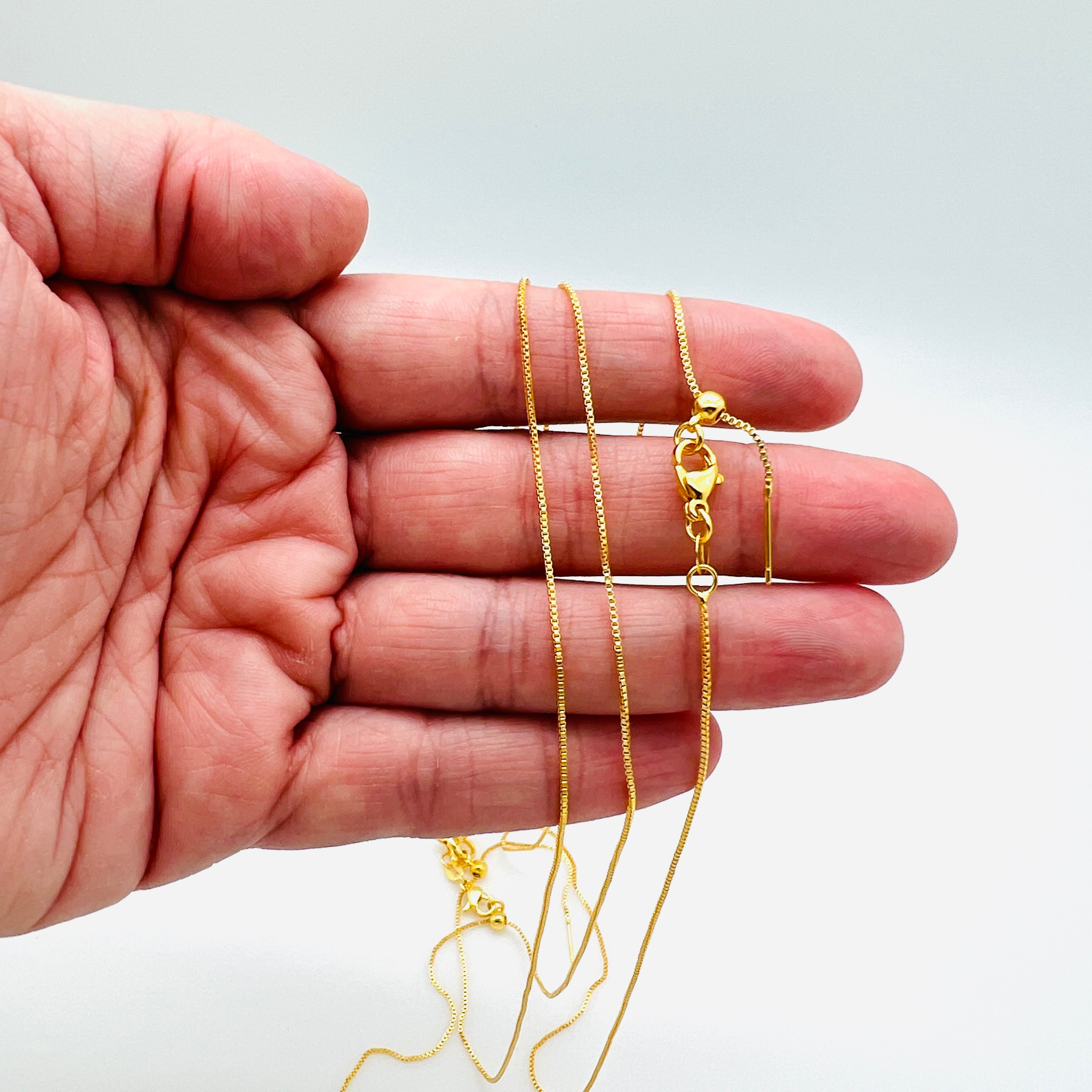 gold plated brass, adjustable box chain with lobster claw clasp shown on a hand with a white background.