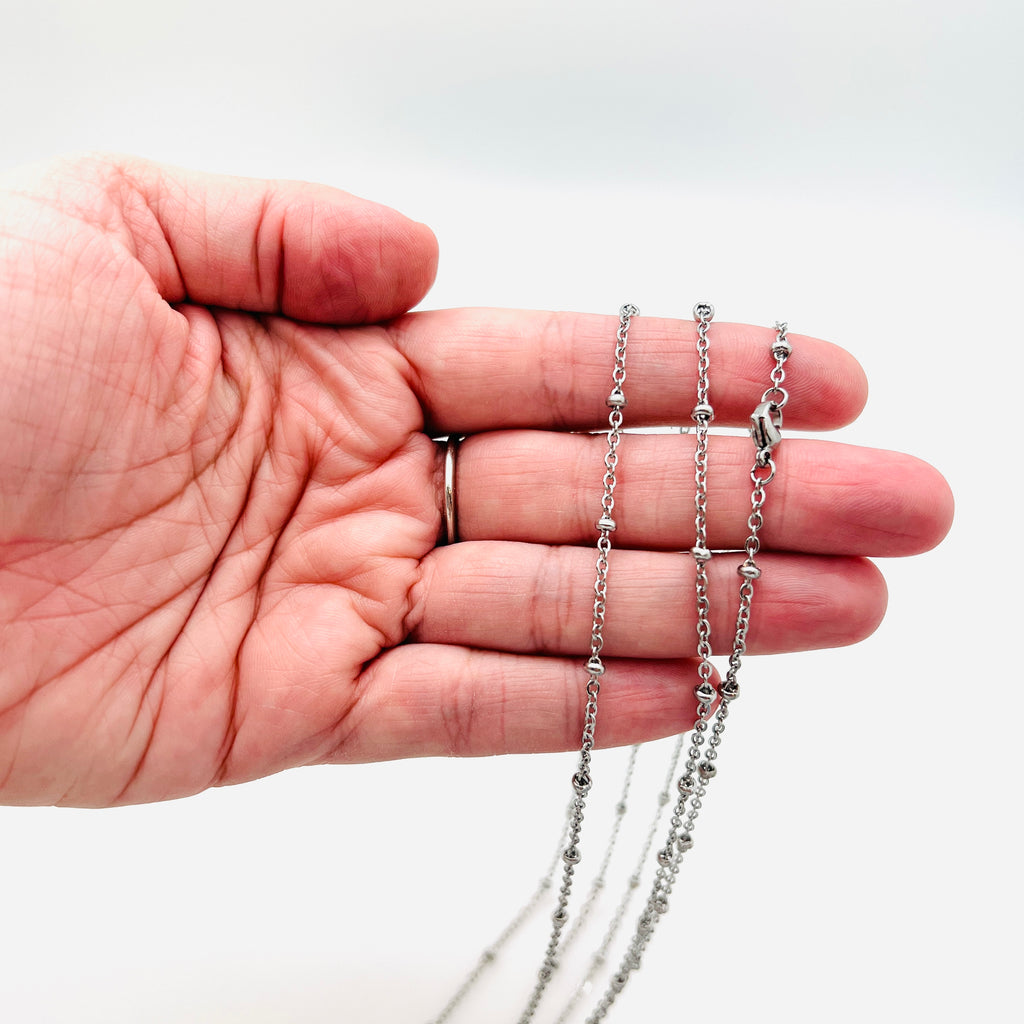 silver tone satellite cable chain necklace with lobster claw clasp draped over hand with white background. 