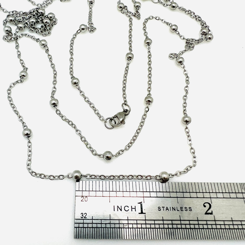stainless steel large bead satellite chain necklace with lobster claw clasp above stainless steel imperial ruler on white background. 