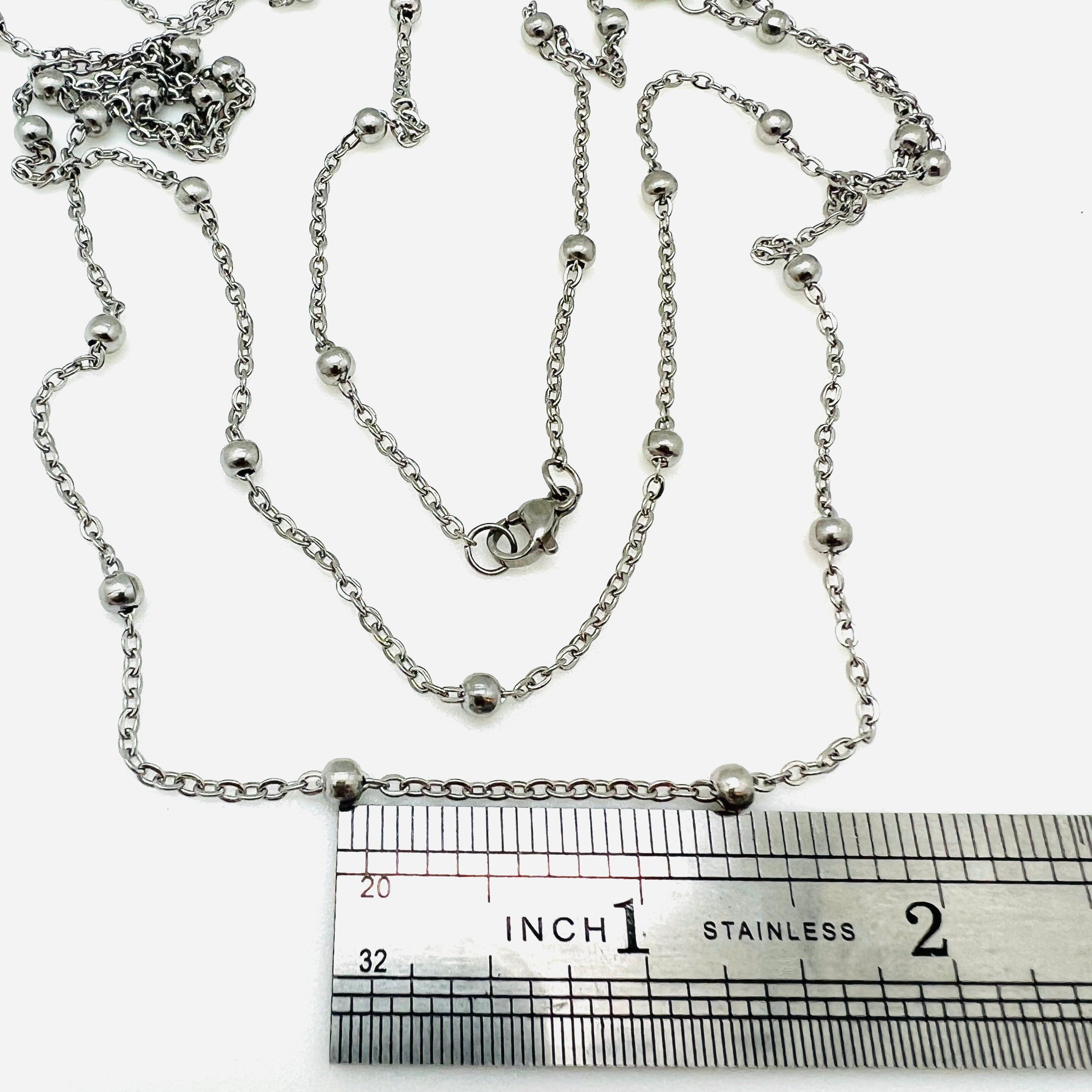 stainless steel large bead satellite chain necklace with lobster claw clasp above stainless steel imperial ruler on white background. 