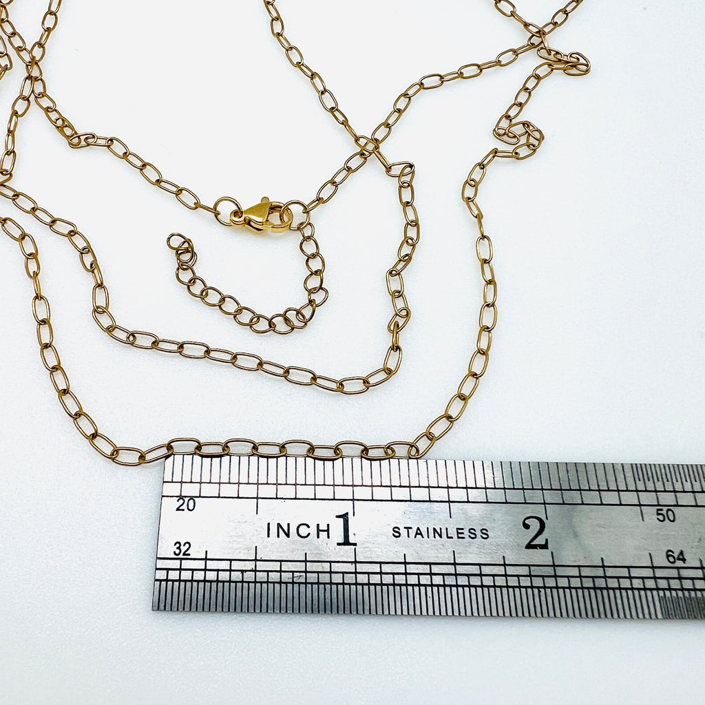 small golden paperclip chain necklace with lobster claw clasp and extender displayed above ruler over white background. 