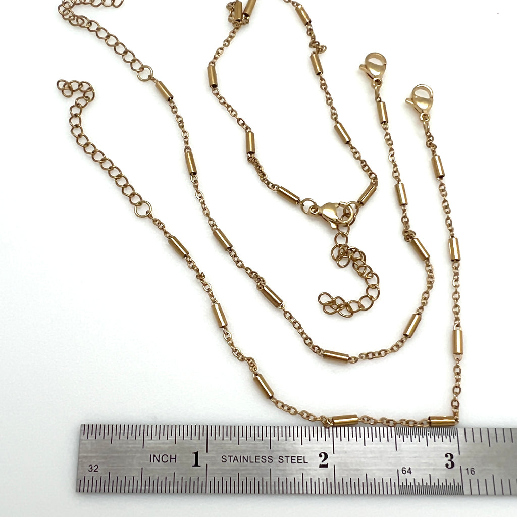 golden satellite tube chain bracelet with lobster claw clasp and extender above a stainless steel imperial ruler against on white background. 