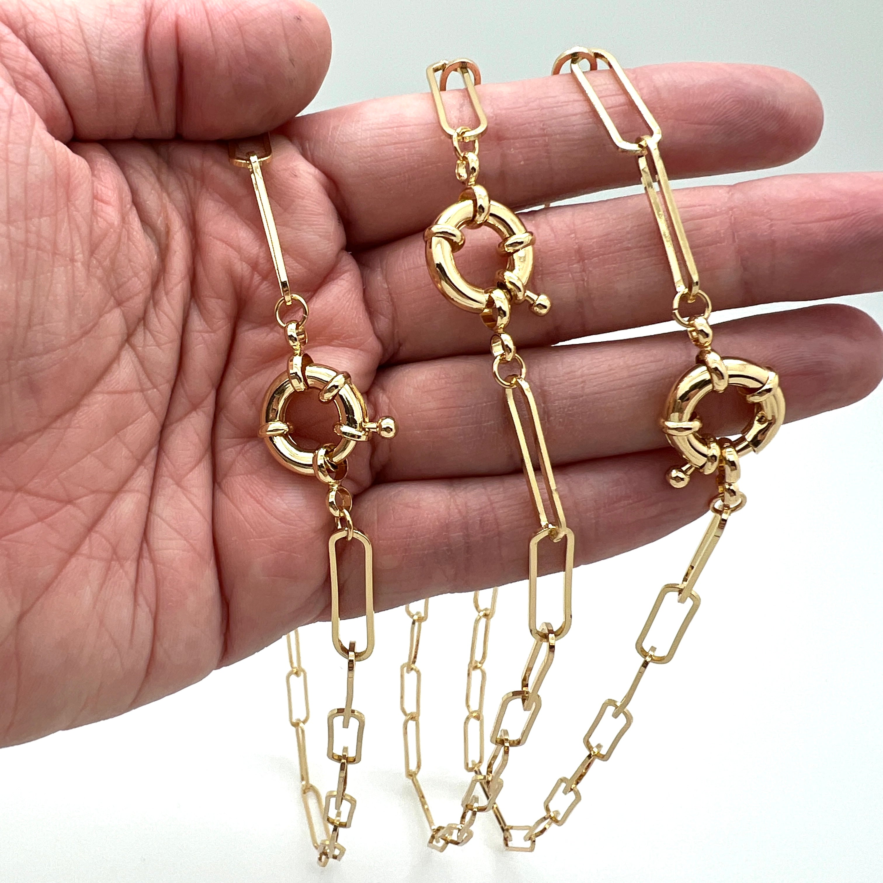 3 golden paperclip chain necklaces with large spring ring clasp draped over  a hand against white background. 