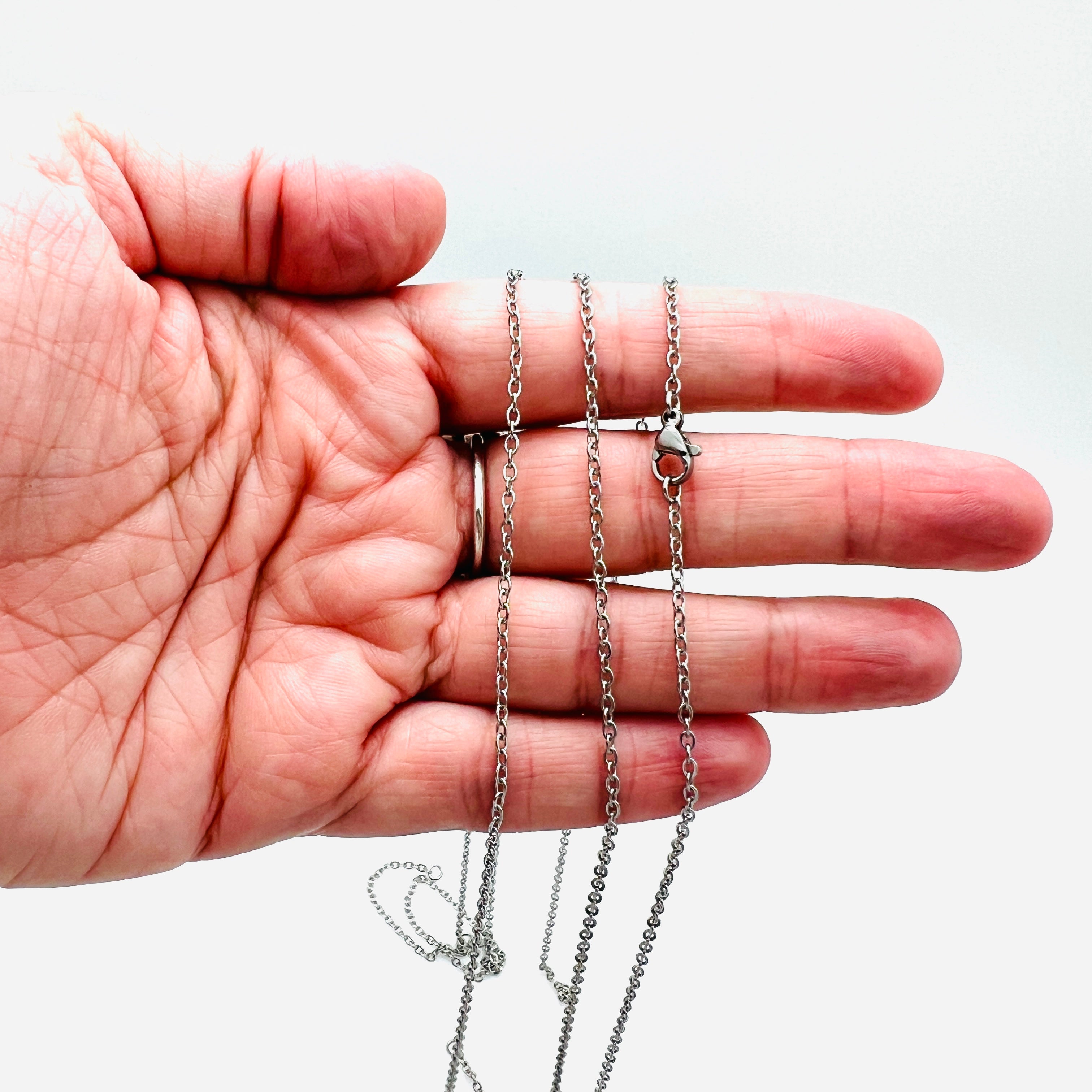 stainless steel cable chain necklace separated in the center with two jump rings ready to attach your favorite connector and a lobster claw clasp draped over a hand against a white background. 