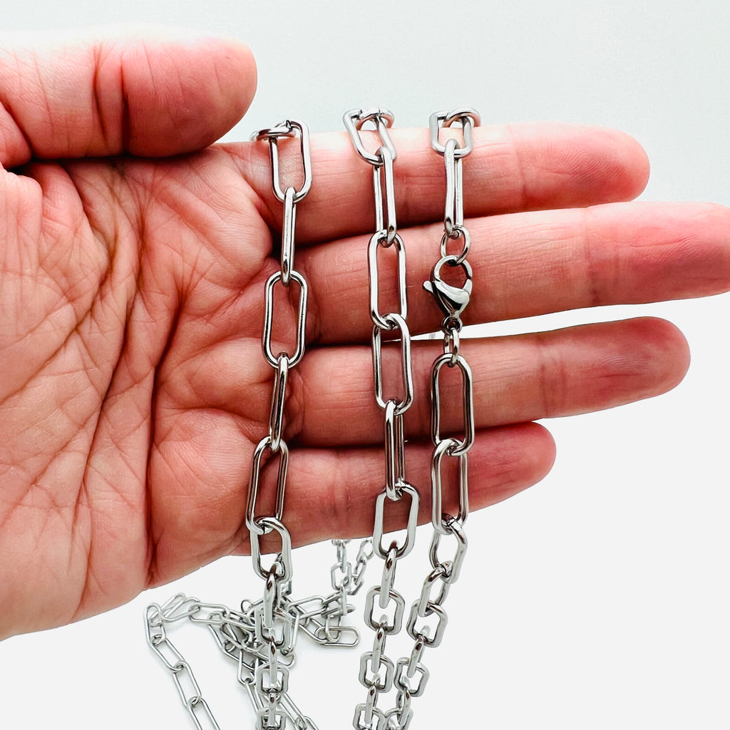 silver tone rounded paperclip chain with lobster claw clasp draped over hand against a white background. 