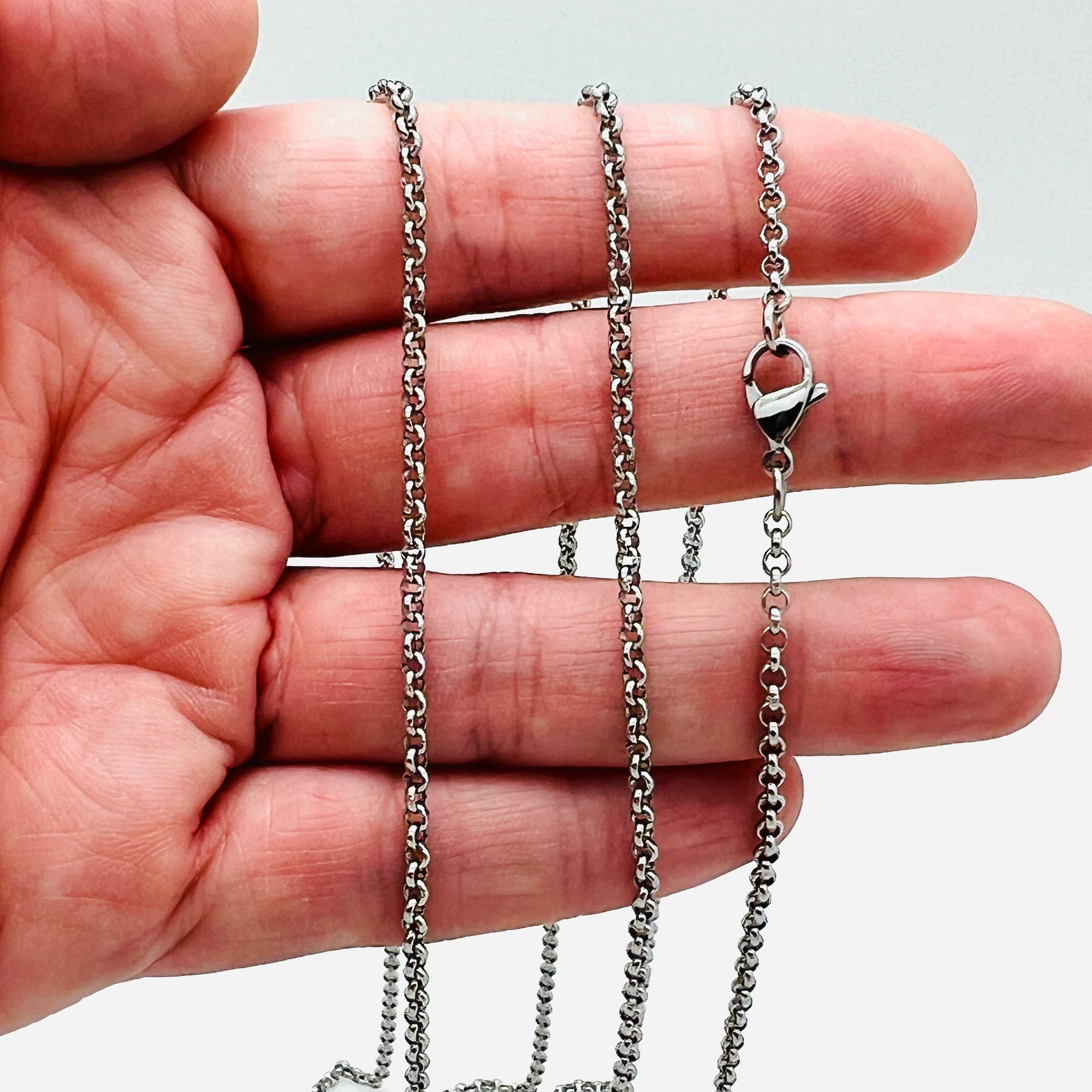 silver tone Rolo chains necklace with lobster claw clasp draped over a hand against a white background. 