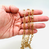 golden paperclip link chain necklace with lobster claw clasp displayed on a hand with a white background. 