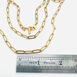 golden medium link paperclip chain necklace with lobster claw clasp above stainless steel imperial ruler on white background. 