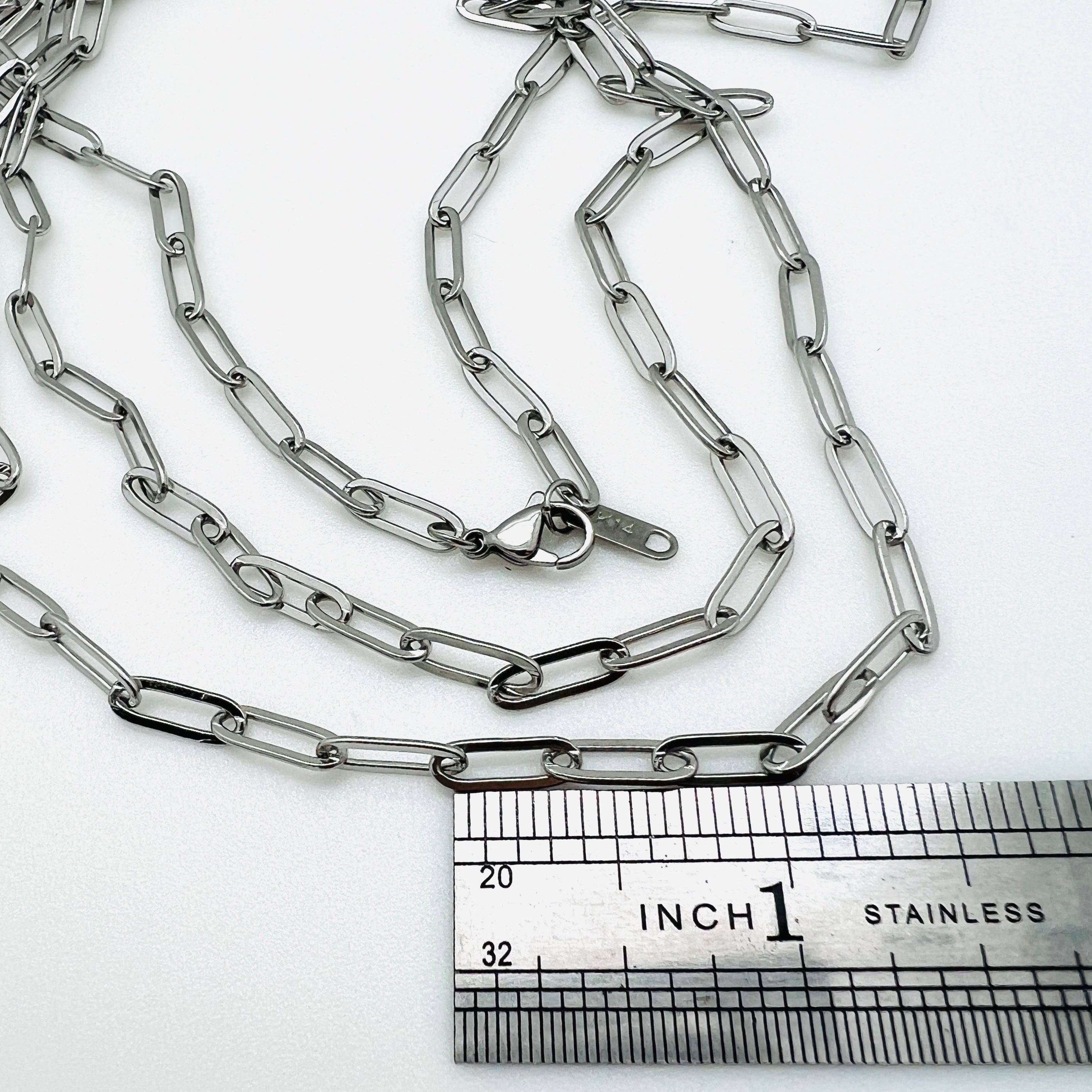 silver tone medium link paperclip chain necklace with lobster claw clasp above stainless steel ruler on white background. 