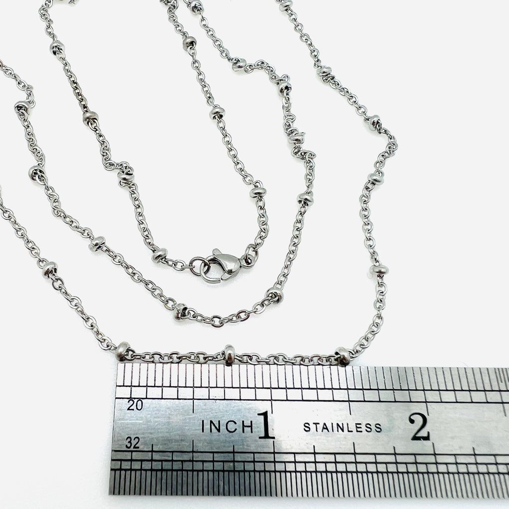 silver tone satellite cable chain necklace with lobster claw clasp displayed over rule on white background. 