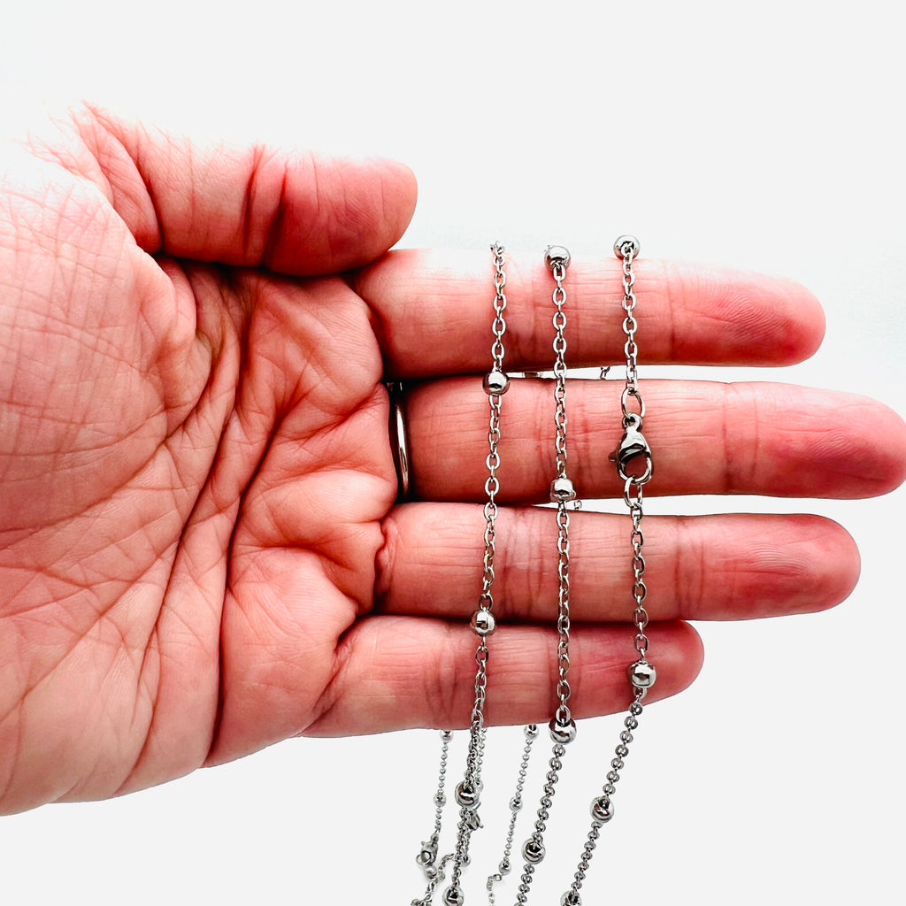 stainless steel large bead satellite chain necklace with lobster claw clasp displayed on a hand with white background. 