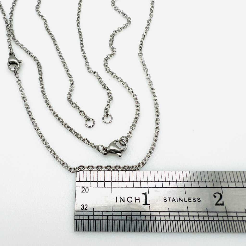 stainless steel cable chain necklace separated in the center with two jump rings ready to attach your favorite connector and a lobster claw clasp displayed above a stainless steel ruler  against a white background. 