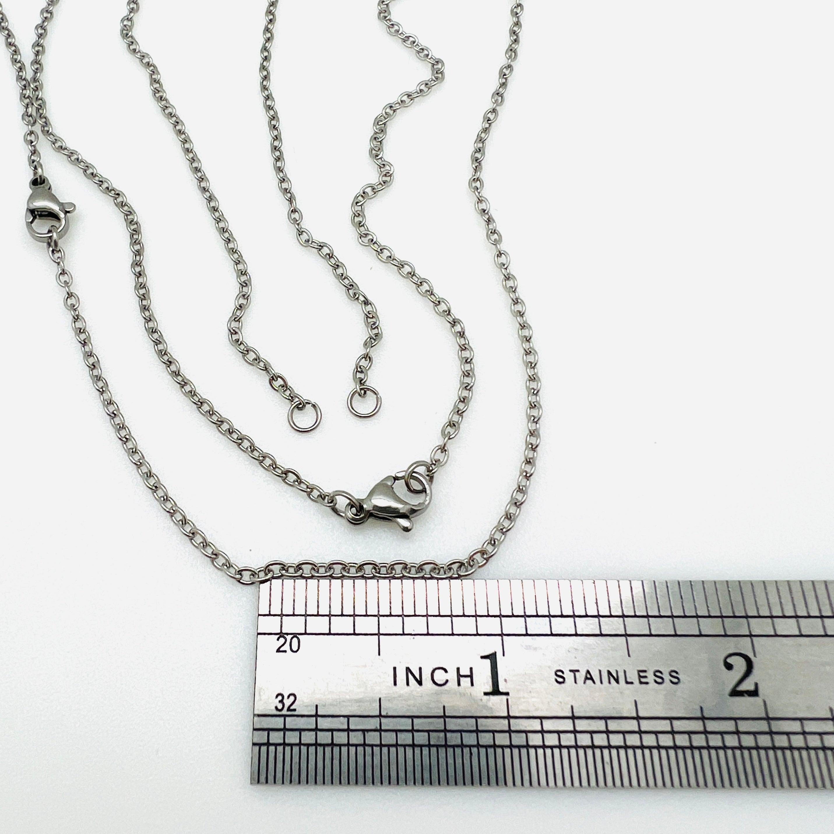 stainless steel cable chain necklace separated in the center with two jump rings ready to attach your favorite connector and a lobster claw clasp displayed above a stainless steel ruler  against a white background. 