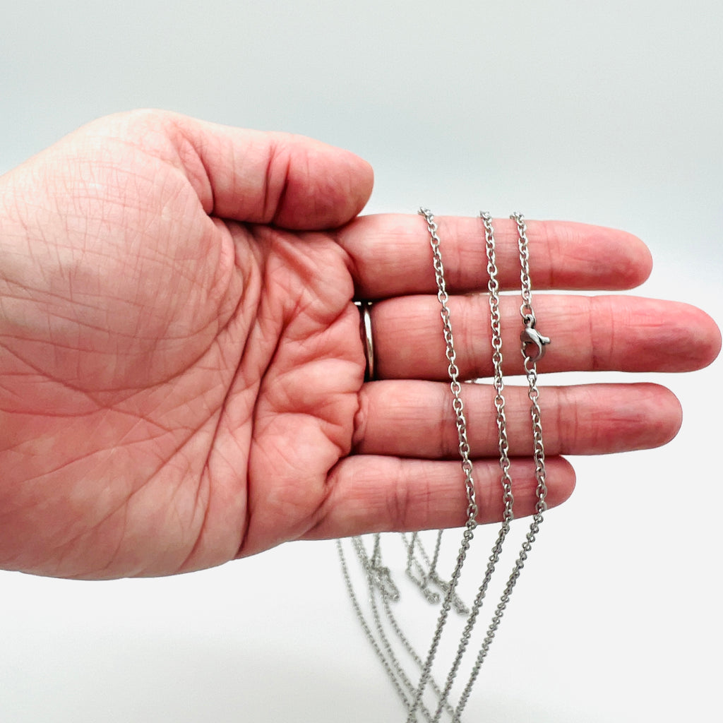 silver tone cable chain necklace with lobster claw clasp draped over a hand against white background. 