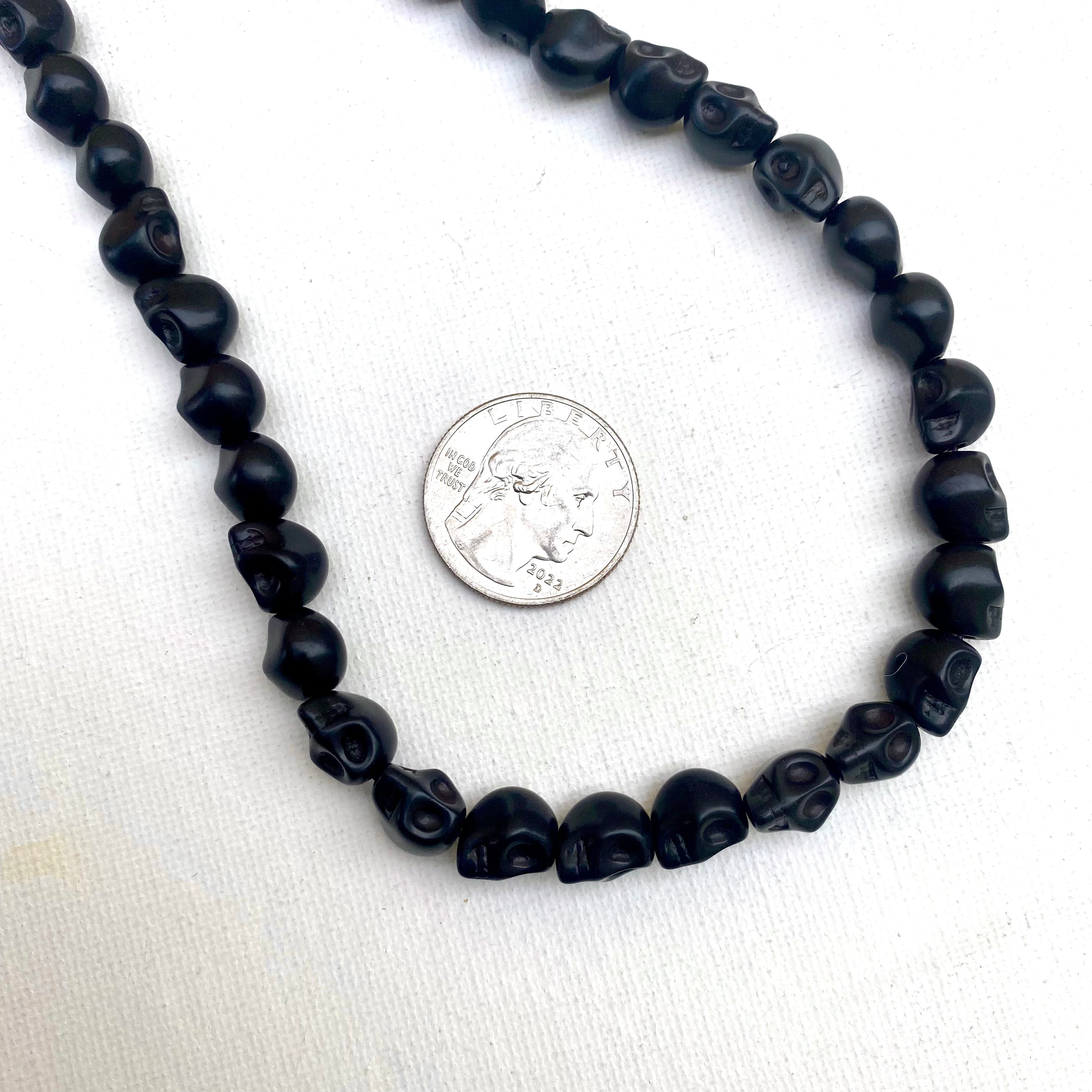 black skull carved stone bead strand next to a quarter for size on white background. 