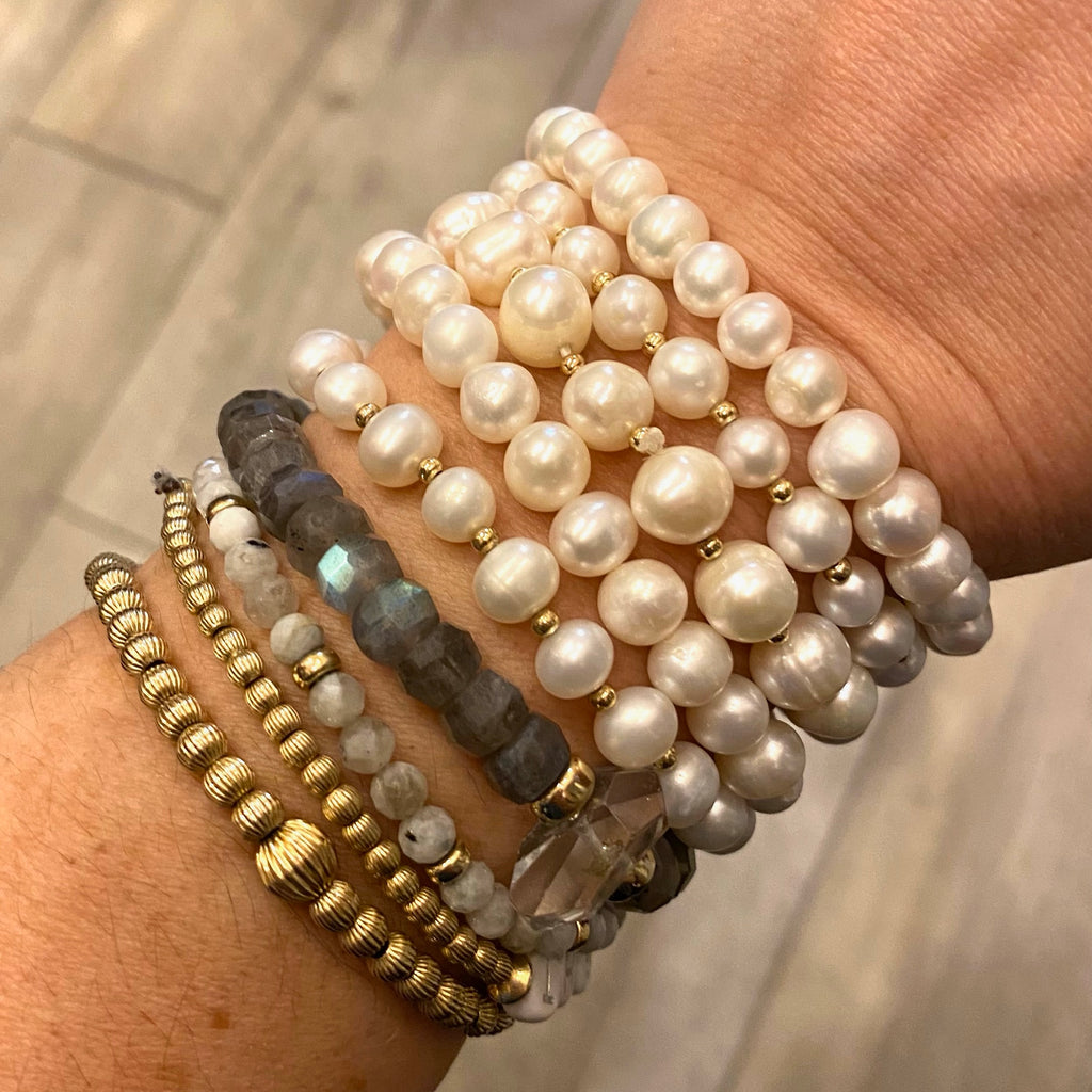 photo of multi-bracelet stack on human wrist including from left to right, two antique bead stretchy bracelets then two natural stone stretchy bracelets and five pearl stretchy bracelets. 