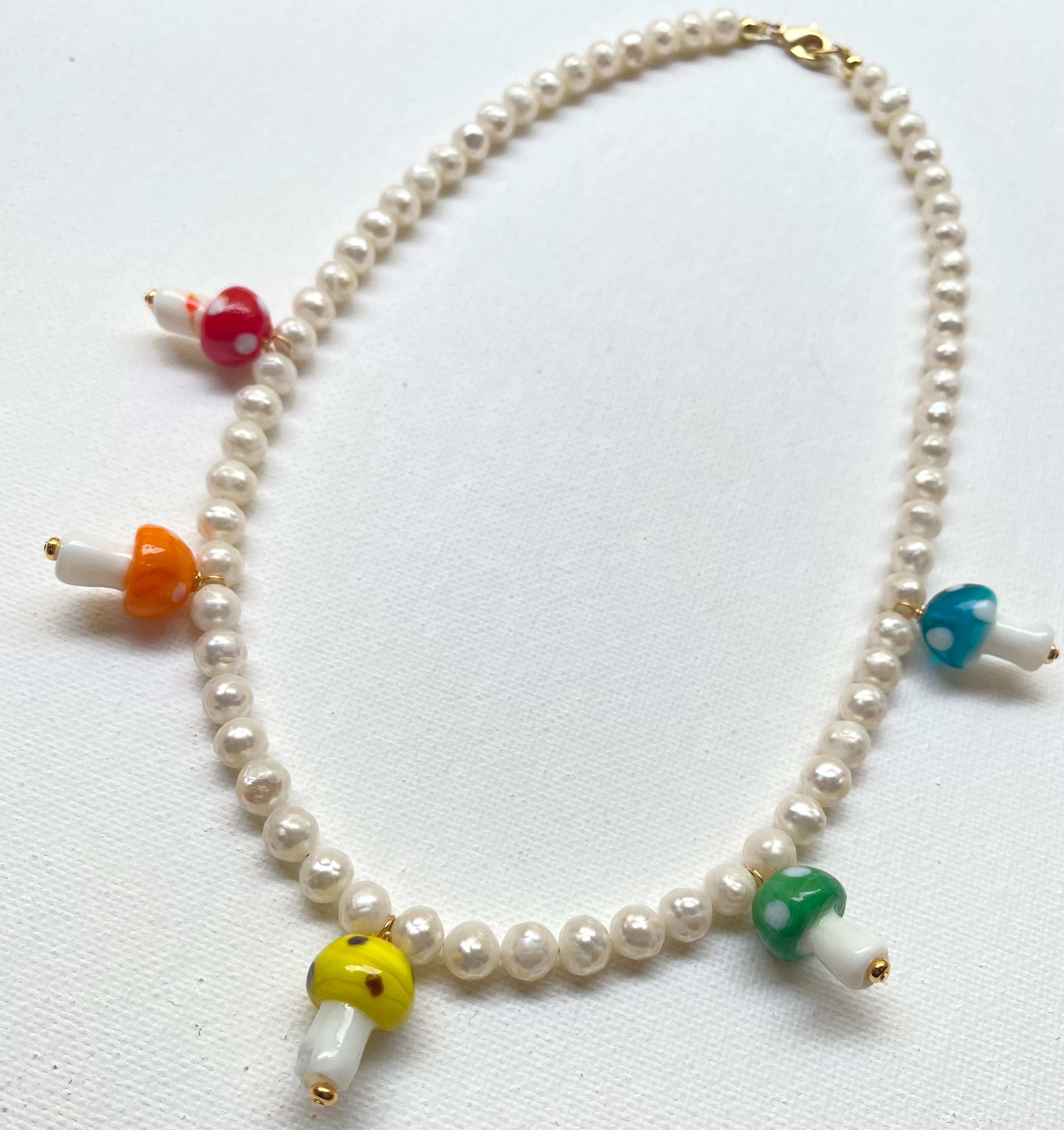 red, orange, yellow, green, and blue glass mushroom beads on a white pearl necklace with a gold clasp on a white background