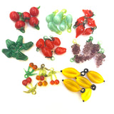 red glass creole tomatoes, green glass pears, red glass strawberries, green glass bell peppers, red glass berries, purple glass grapes, red glass cherries, and yellow glass bananas on a white background