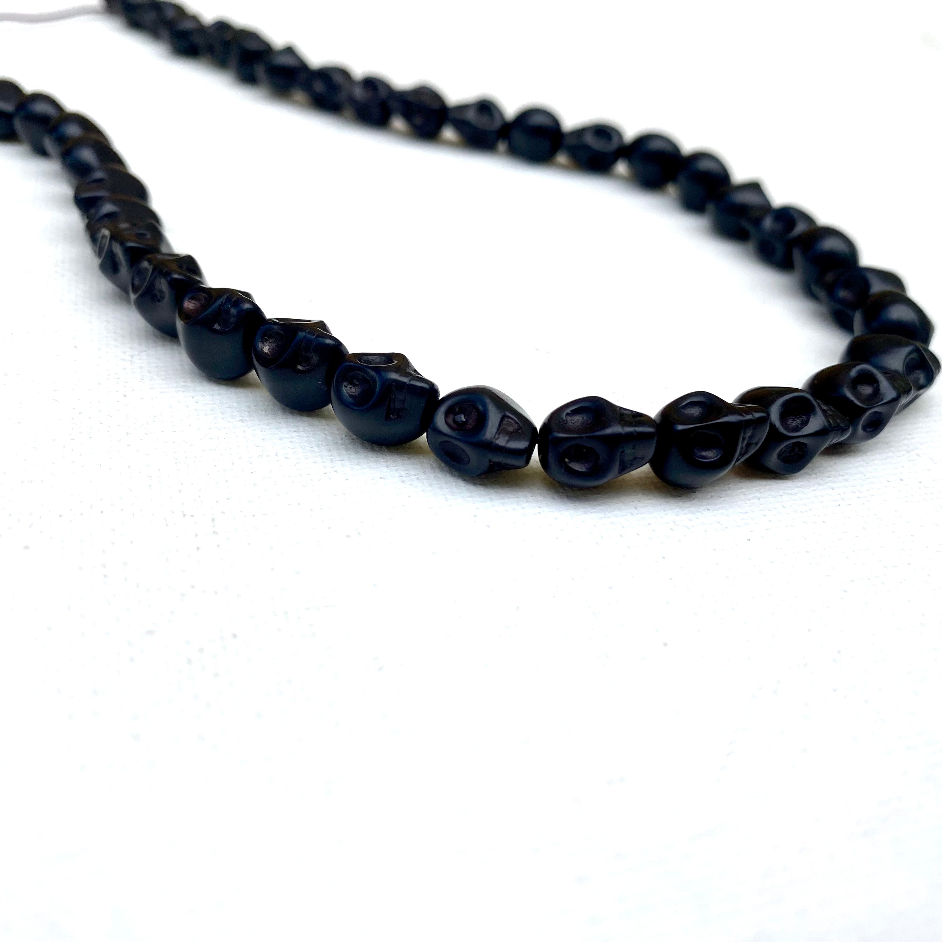 black skull carved stone bead strand on white background. 