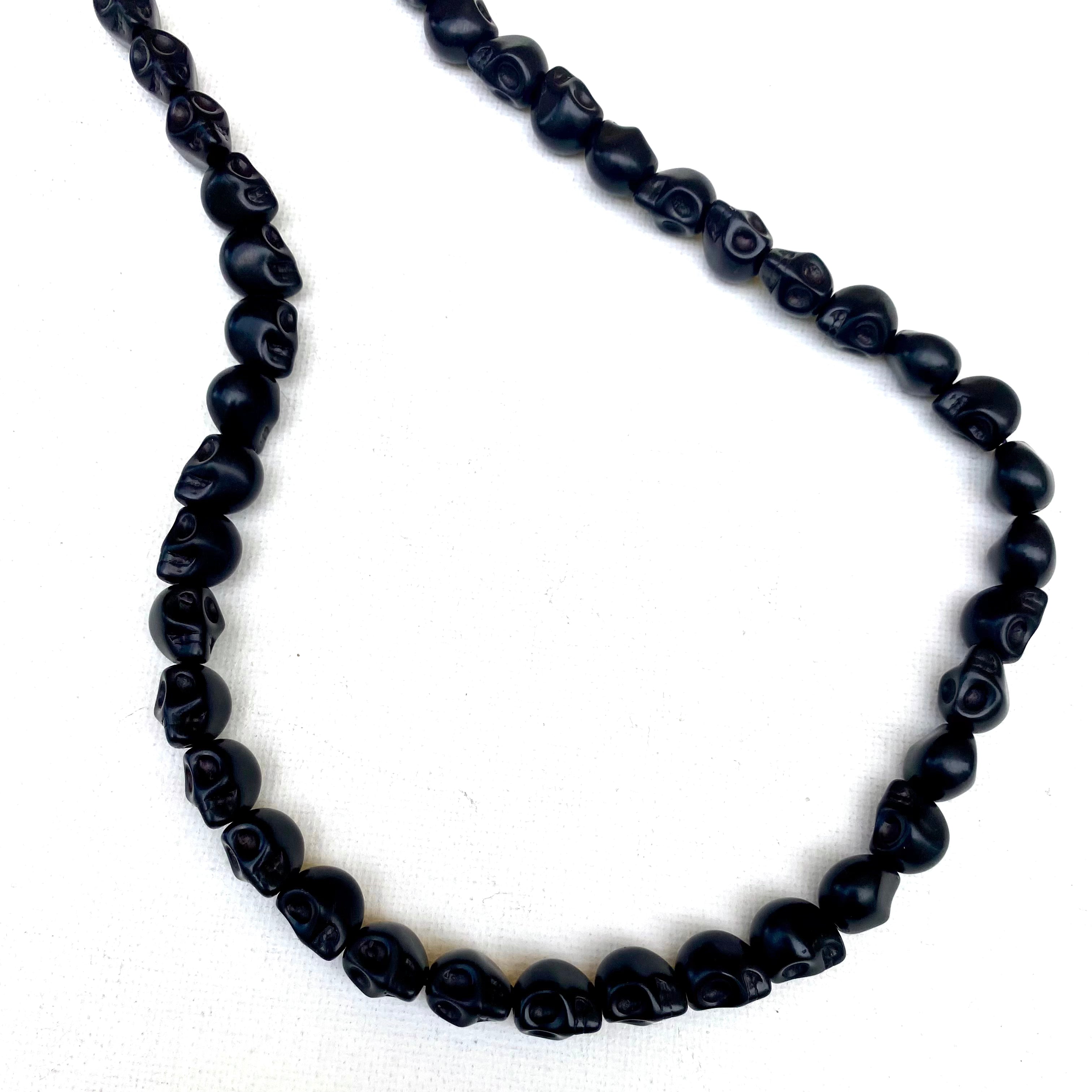 black skull carved stone bead strand on white background. 