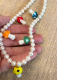 red, orange, yellow, green, and blue glass mushroom beads on a white pearl necklace with a gold clasp on a womans hand to represent scale 