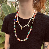 short multi-color mushroom and pearl necklace and long multi-color necklace being worn by a lady with a black shirt in front of a green background