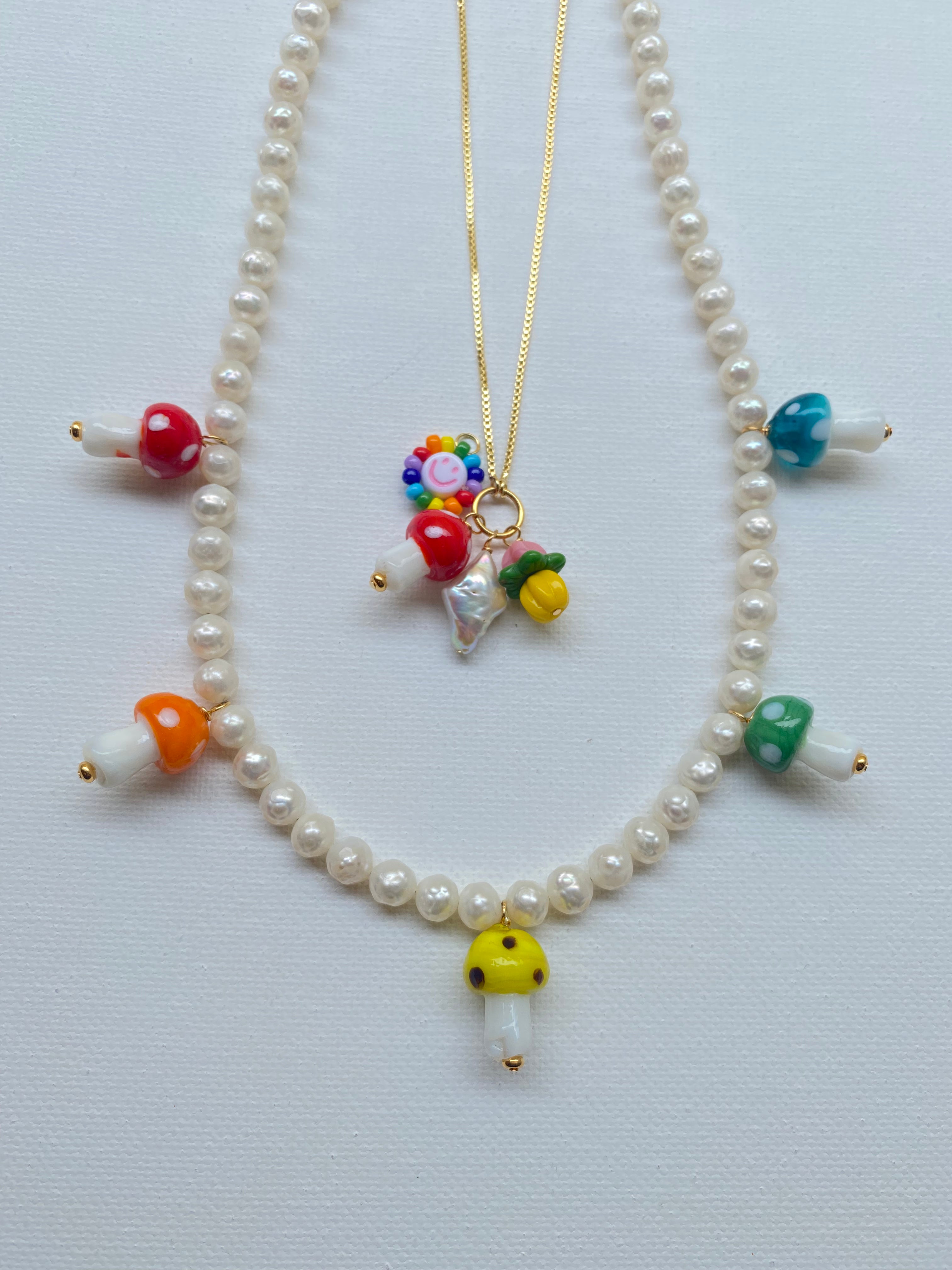 red, orange, yellow, green, and blue glass mushroom beads on a white pearl necklace with a gold clasp on a white background