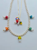 red, orange, yellow, green, and blue glass mushroom beads on a white pearl necklace with a gold clasp on a white background