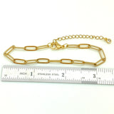 golden paperclip chain bracelet with lobster claw clasp and extender chain with bezel set clear stone on end above a stainless steel imperial ruler on a white background.