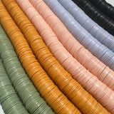 close-up photo of sage green, mustard yellow, pale pink, blue-grey, and black vinyl disk beads