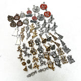 collection of 60 charms on a white background. Charms include copper, bronze, silver, and orange enamel jack-o-lanterns (pumpkins), silver, gold and white enamel ghost charms, silver Devil charms, gold and silver witch charms, gold and silver broom charms, gold and silver kiss candy charms, gold and silver cat charms, gold and silver trick-or-treat baskets, gold and silver haunted house charms and silver candy charms