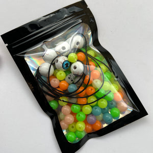 bag of multi-color glow in the dark beads with black elastic beading cord and wooden eyeball beads on white background